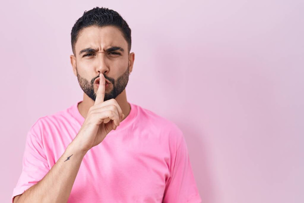 Hispanic young man standing over pink background asking to be quiet with finger on lips. silence and secret concept.  - Photo, Image