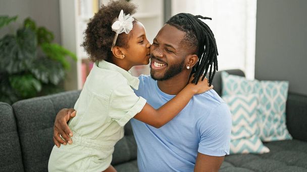 Afrikai amerikai apa és lánya magabiztosan mosolyogva ölelgetik egymást otthon a kanapén csókolózva. - Fotó, kép
