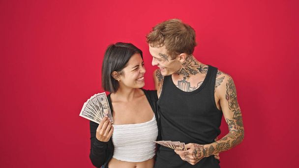 Kaunis pari halaamassa toisiaan pitäen dollareita hymyillen eristetyllä punaisella taustalla - Valokuva, kuva