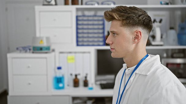 Atractivo joven caucásico, un científico concentrado, mirando a un lado en el laboratorio durante una intensa sesión de análisis biológico - Foto, Imagen