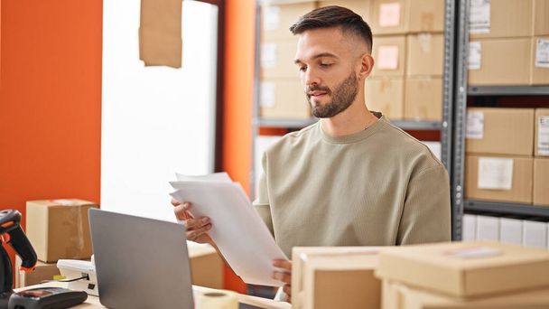 Fiatal spanyol férfi e-kereskedelmi üzleti használ laptop olvasási dokumentumot az irodában - Fotó, kép