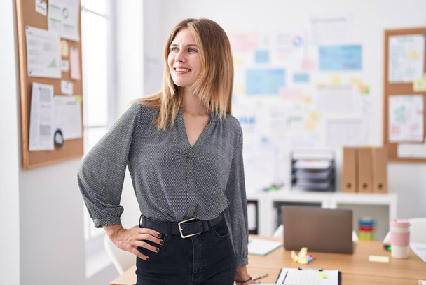 Молодая блондинка бизнес-работница улыбается уверенно стоя на своем посту - Фото, изображение