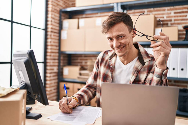 Jeune homme ecommerce travailleur d'affaires en utilisant l'écriture d'ordinateur portable sur le document au bureau - Photo, image