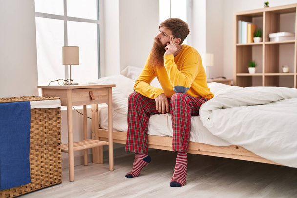 Молодой рыжий мужчина стресс сидя на кровати в спальне - Фото, изображение