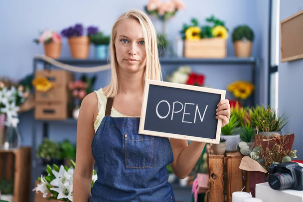 Young caucasian woman working at florist with open sign thinking attitude and sober expression looking self confident  - Photo, Image