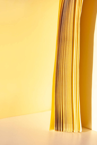 Ola de papel amarillo de páginas sobre fondo beige con sombra. Espacio para el texto. Copiar espacio - Foto, Imagen