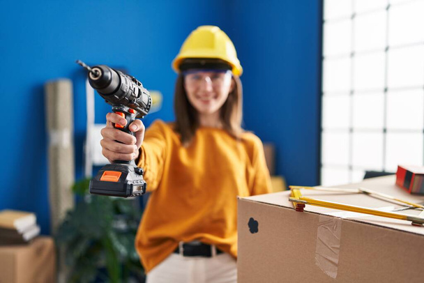 Young blonde woman wearing hardhat holding drill at new home - Photo, Image