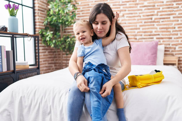 Mother and son sitting on bed preparing child wearing clothes at bedroom - Photo, Image