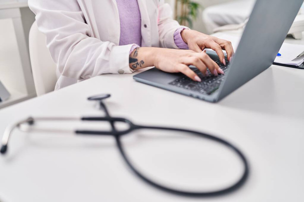 młoda kaukaska kobieta lekarz za pomocą laptop siedzi na stole w klinice - Zdjęcie, obraz