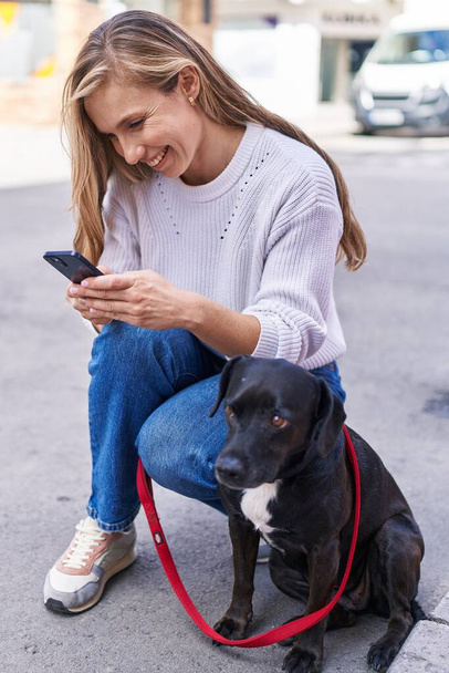 若いですブロンド女性使用スマートフォン立って犬によって通り - 写真・画像