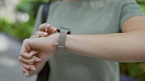 Momento cautivador de una mujer parada al aire libre en el parque de la ciudad, sus manos tocando tiernamente las manos de su reloj de pulsera - Foto, Imagen