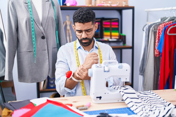 Jovem árabe homem alfaiate estressado usando máquina de costura na loja de alfaiate - Foto, Imagem