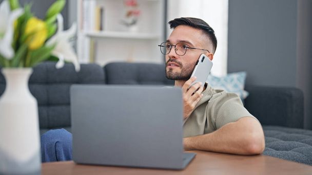 Молодий іспаномовний чоловік розмовляє по смартфону за допомогою ноутбука вдома
 - Фото, зображення