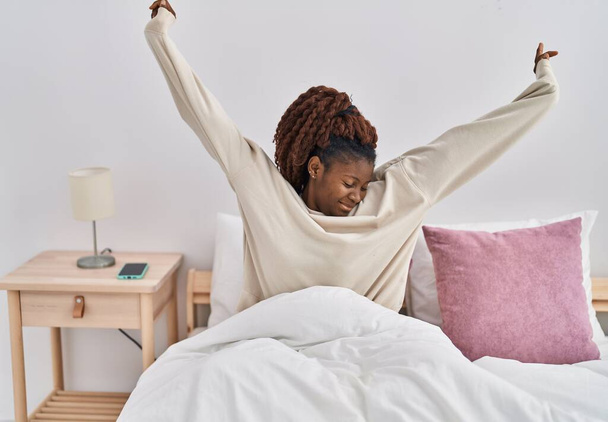 African american woman waking up stretching arms at bedroom - Photo, Image