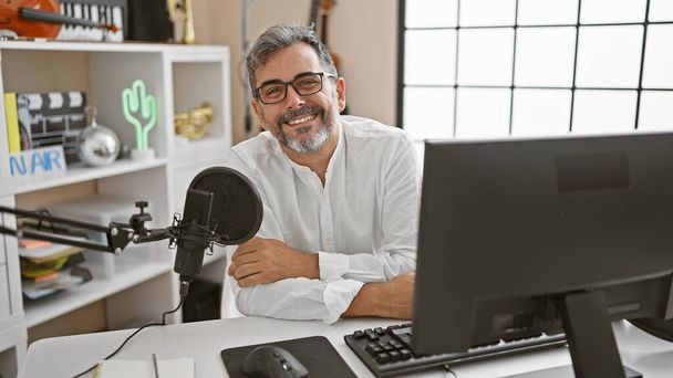 Молодий, привабливий, сіроволосатий іспаномовний чоловік посміхається і майстерно представляє новини в прямому ефірі радіошоу всередині професійної радіостудії - Фото, зображення