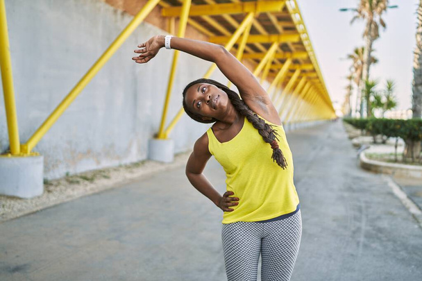 African american woman wearing sportswear stretching arm at street - Фото, зображення