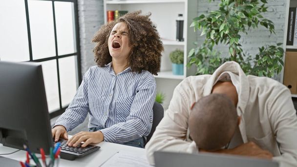 Uitgeputte mannelijke en vrouwelijke collega 's werken onvermoeibaar op de computer, twee vermoeide kantoormedewerkers vechten tegen het gazon binnen - Foto, afbeelding