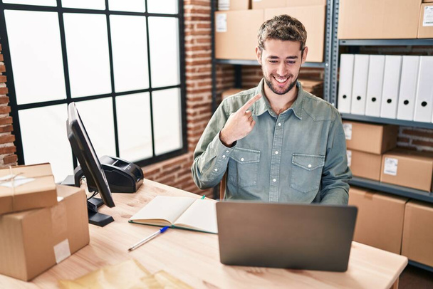 Hombre hispano con barba trabajando en el comercio electrónico de pequeñas empresas sonriendo feliz señalando con la mano y el dedo  - Foto, Imagen