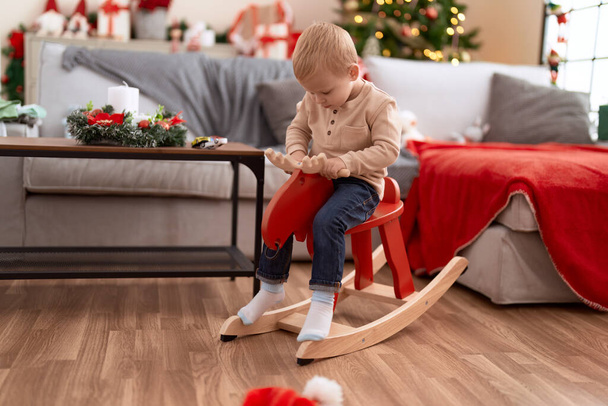 Adorable toddler playing on reindeer rocking by christmas tree at home - Photo, Image