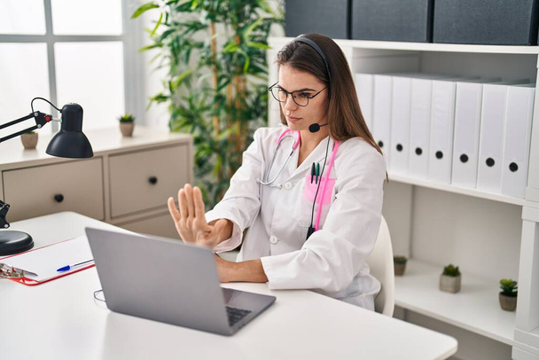 Красивая женщина врач работает на онлайн-встречи с открытой рукой делать стоп-знак с серьезным и уверенным выражением, защитный жест  - Фото, изображение