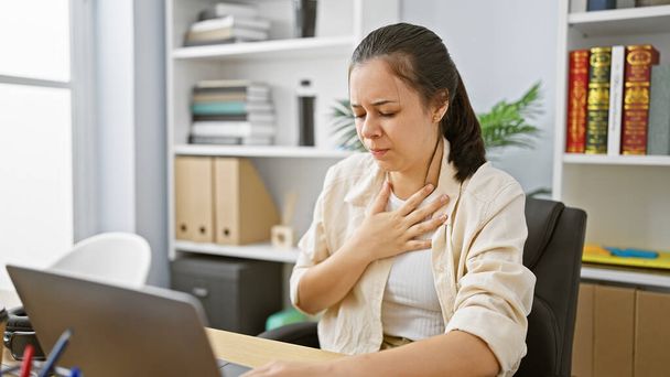 Attacco di tosse colpisce bella giovane donna ispanica mentre lavora duramente al suo lavoro in ufficio tra preoccupazioni coronavirus - Foto, immagini