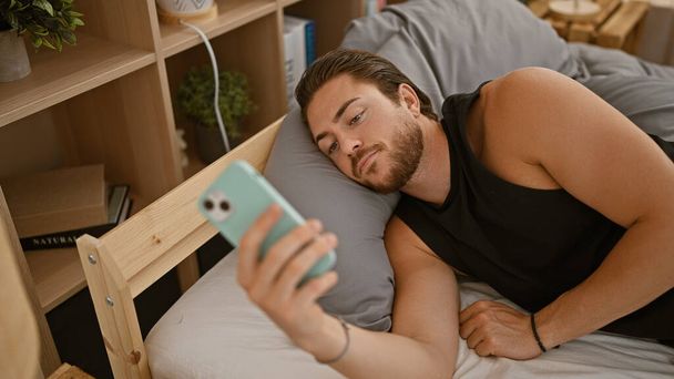 Genç İspanyol adam yatakta akıllı telefon kullanıyor. - Fotoğraf, Görsel