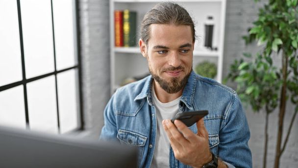 Молодой латиноамериканец-бизнесмен отправляет голосовое сообщение на смартфон, работающий в офисе - Фото, изображение