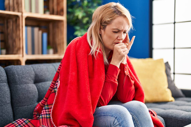 Young blonde woman sitting on sofa coughing at home - Photo, Image