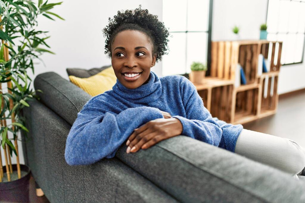Afrikkalainen amerikkalainen nainen hymyilee luottavainen istuu sohvalla kotona - Valokuva, kuva