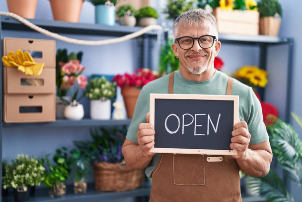 Hispanic man with grey hair working at florist holding open sign smiling with a happy and cool smile on face. showing teeth.  - Photo, Image