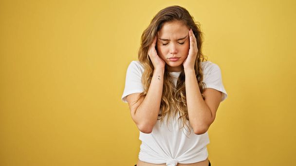 Jonge mooie Latijns-Amerikaanse vrouw lijden aan hoofdpijn over geïsoleerde gele achtergrond - Foto, afbeelding