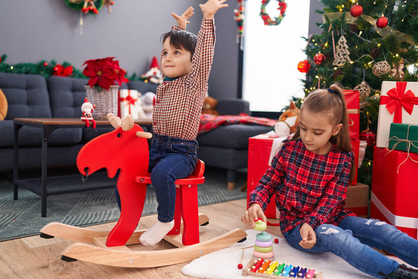 Imádnivaló fiú és lány játszik rénszarvas rocking és játék ünnepli karácsonyi otthon - Fotó, kép