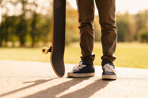 Nahaufnahme von Schuhen und Skateboard im Park bei Sonnenuntergang. - Foto, Bild