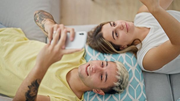 自宅でソファーに横たわっているスマートフォンを使用して美しいカップル - 写真・画像