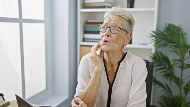 Senior donna dai capelli grigi operaia in ufficio, mal di denti dolori sciopero durante la giornata lavorativa - Foto, immagini