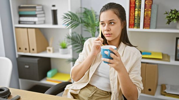 Jovem bela mulher hispânica empresária falando no smartphone bebendo café no escritório - Foto, Imagem