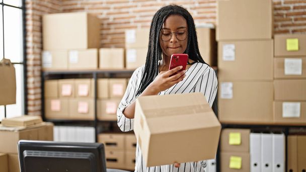 Paquete de escaneo de trabajador de negocios de comercio electrónico de mujer afroamericana con teléfono inteligente en la oficina - Foto, imagen
