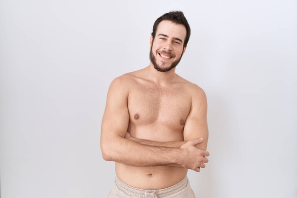 Νεαρός Ισπανόφωνος στέκεται γυμνός πάνω από λευκό φόντο χαρούμενο πρόσωπο χαμογελώντας με σταυρωμένα τα χέρια κοιτάζοντας την κάμερα. θετικό πρόσωπο.  - Φωτογραφία, εικόνα