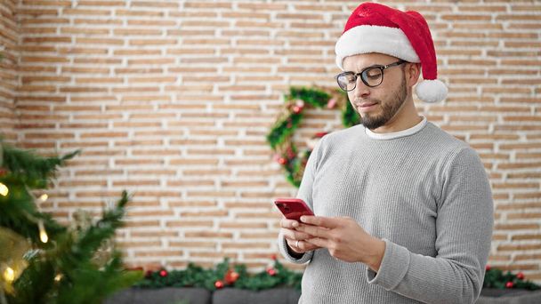 Іспаномовний чоловік у різдвяній шапці використовує смартфон вдома - Фото, зображення