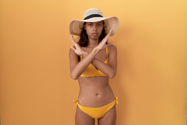Jeune femme hispanique portant un bikini et un chapeau d'été expression de rejet croisant les bras faisant signe négatif, visage en colère  - Photo, image