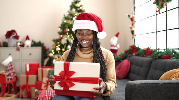 Afrikai nő kicsomagolás ajándék ül karácsonyfa otthon - Fotó, kép