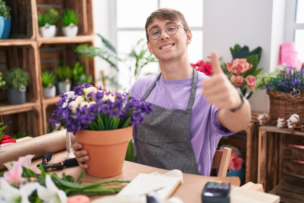 花屋で働く白人ブロンドの男性は,手で肯定的なジェスチャーをすることを承認し,笑顔で幸せです. 勝者のジェスチャー.  - 写真・画像