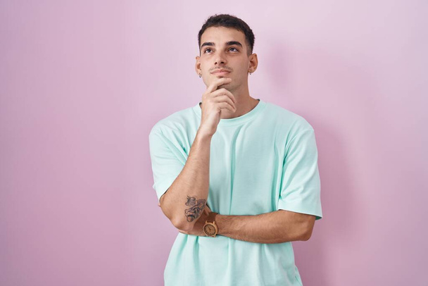 Handsome hispanic man standing over pink background with hand on chin thinking about question, pensive expression. smiling with thoughtful face. doubt concept.  - Photo, Image