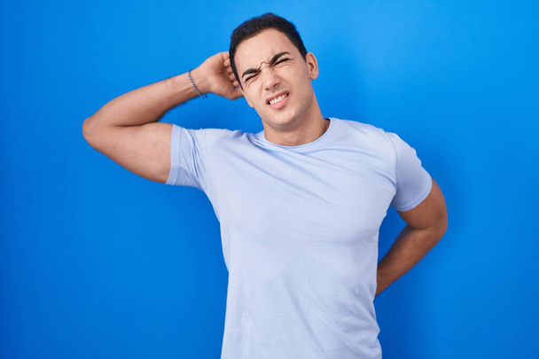 Young hispanic man standing over blue background stretching back, tired and relaxed, sleepy and yawning for early morning  - Photo, Image