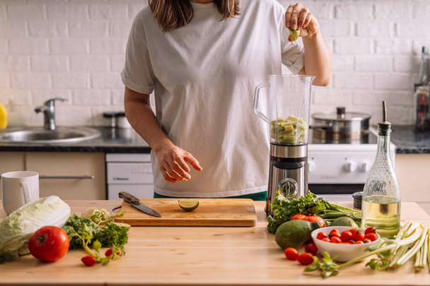 Mutfaktaki kadın taze sebzelerin olduğu ahşap bir masada limonu miksere bastırıyor.. - Fotoğraf, Görsel