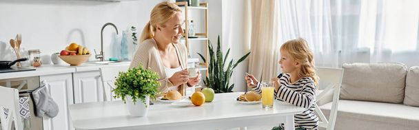 linda chica desayunando con la madre rubia feliz en la cocina moderna, bandera de estilo de vida - Foto, imagen