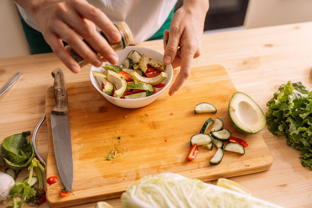 Lady streut Gewürze auf vegetarischen Salat in einem weißen Teller auf einem Holztisch. - Foto, Bild