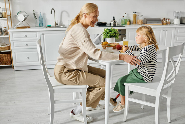 щаслива мати сніданок зі своєю маленькою донькою з протезною ногою на кухні, включення - Фото, зображення