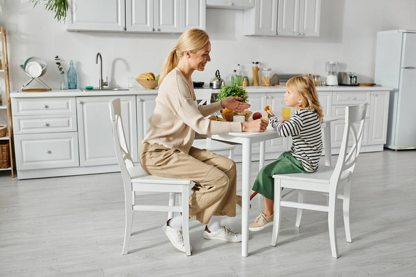 feliz madre desayunando con su hijita con prótesis en la cocina, inclusión - Foto, imagen