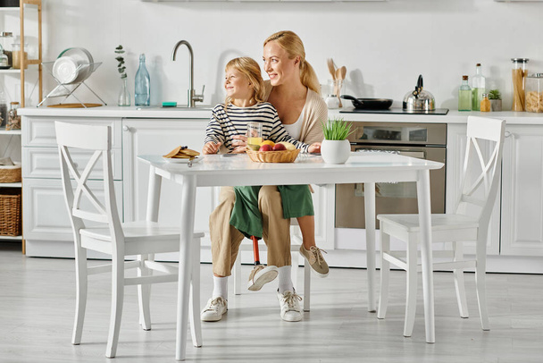 esikoululainen tyttö proteesilla jalka istuu kierroksilla onnellinen äiti aamiaisen aikana keittiössä - Valokuva, kuva